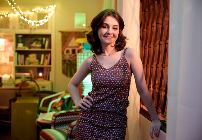 Klara Castanho no set da 3ª temporada de De Volta aos 15 Mulher branca com cabelo médio e castanho olhando para câmera e sorrindo. Ela está vestindo um vestido estampado e com uma mão apoiada na cintura.