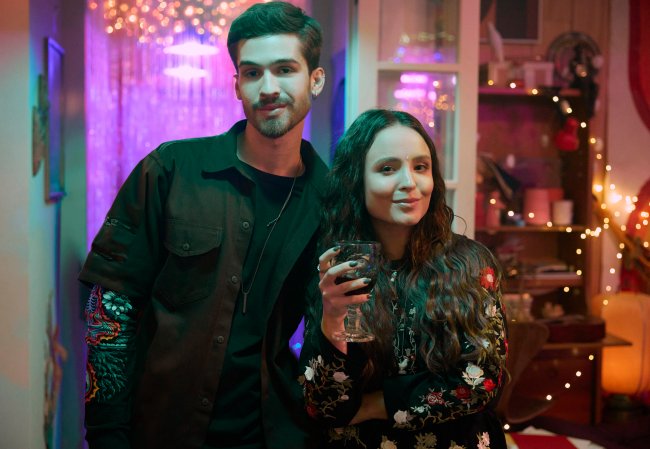 João Guilherme e Larissa Manoela no set da terceira temporada de De Volta aos 15 Homem de roupa preta de lado de mulher com jaqueta estampada e segurando taça de vinho