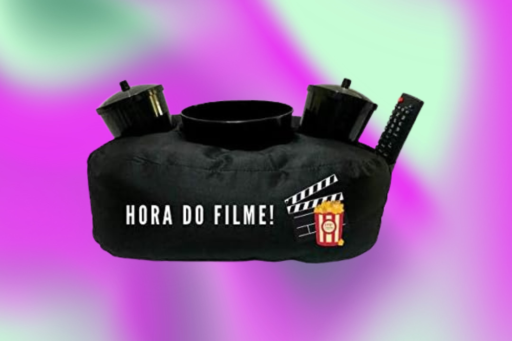 Imagem de uma almofada preta escrito 'hora do filme' no meio, com dois copos, um balde e um controle remoto em cima, em um fundo roxo e verde.