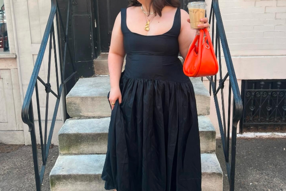 Garota usando vestido preto longo de alças e segurando uma bolsa laranja e um café na mão