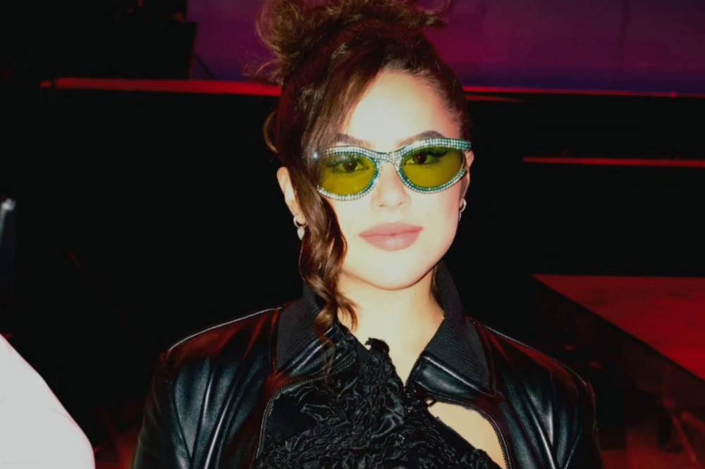 Maisa Silva em festival à noite usando óculos com lentes verdes e jaqueta de couro preta