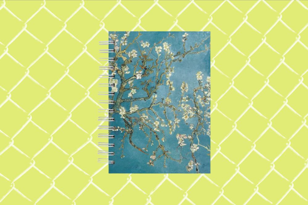 Imagem de um caderno com estampa da pintura de flores do Van Gogh em um fundo amarelo com grades brancas.
