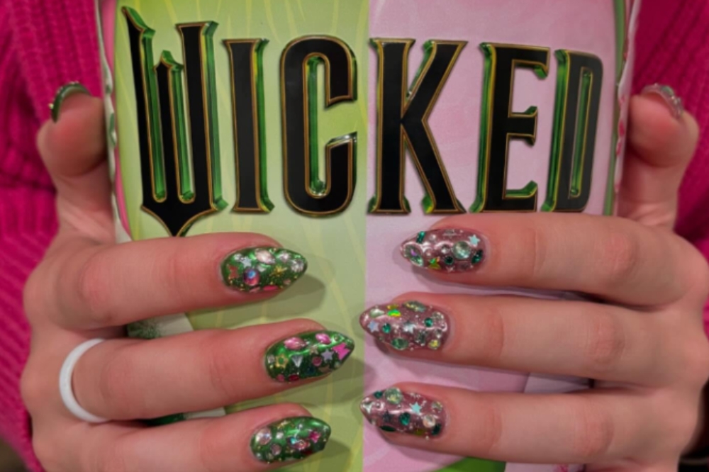 Mãos de garota segurando balde de pipoca de Wicked com unhas pintadas de verde e rosa