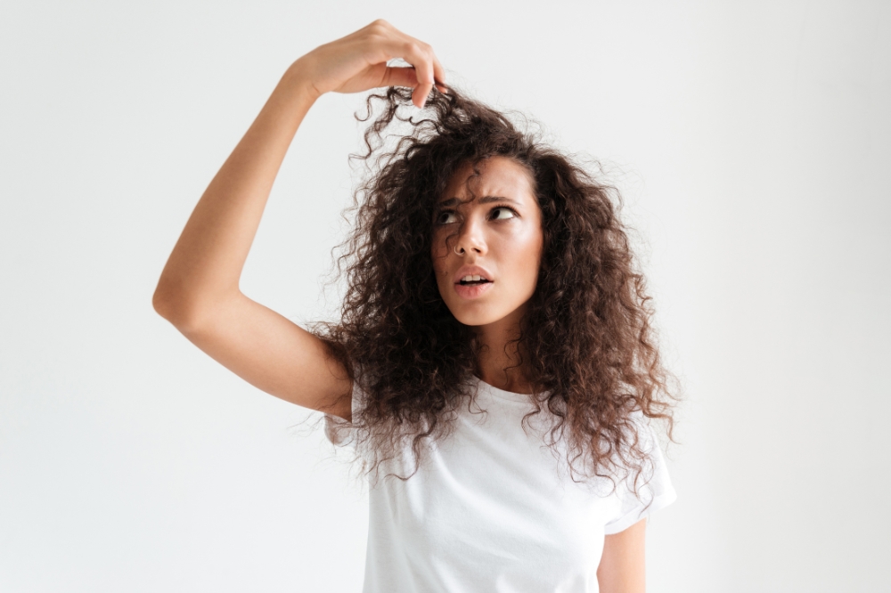 Garota olhando para o cabelo com expressão de estranheza