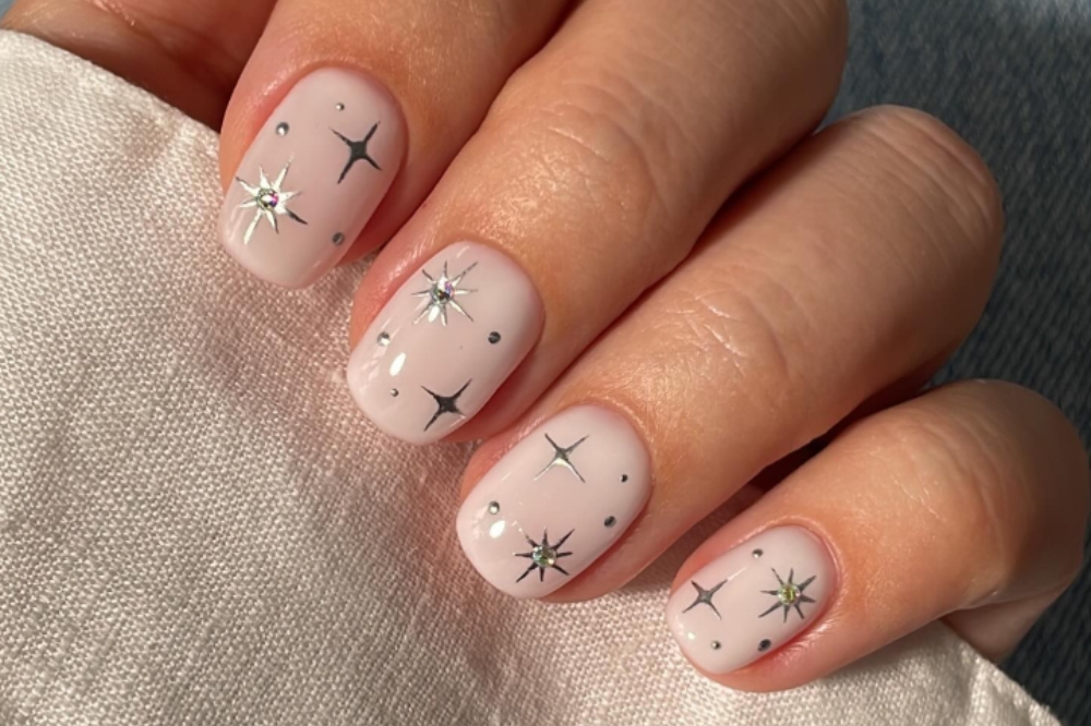 Unha pintada de branco com estrelas prateadas e aplicação de strass