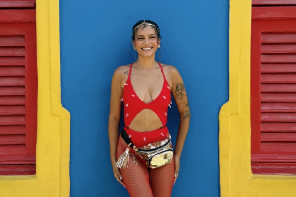 Garota usando look vermelho de Carnaval e pochete dourada na frente de uma parede azul e amarela