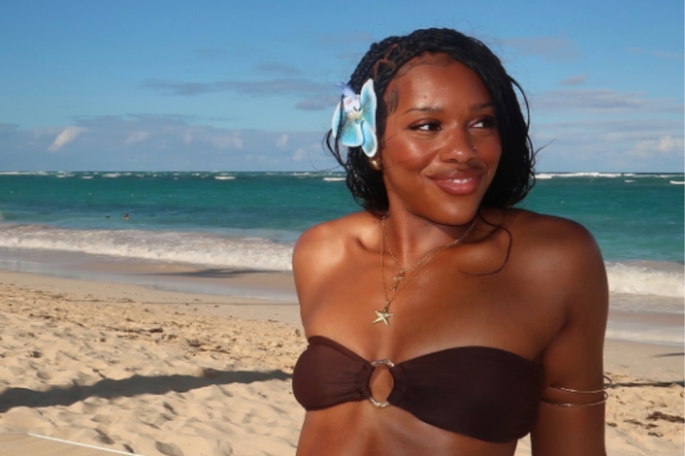 Garota em frente a praia usando biquíni marrom e presilha de flor no cabelo