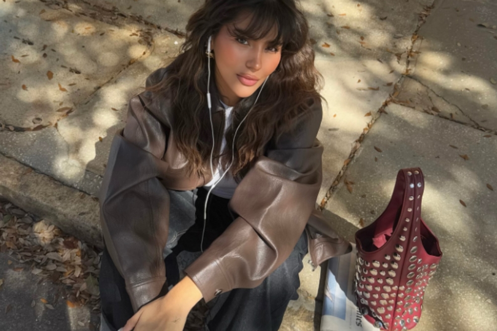 Garota usando jaqueta marrom, camiseta branca, calça jeans e bolsa vermelho cereja