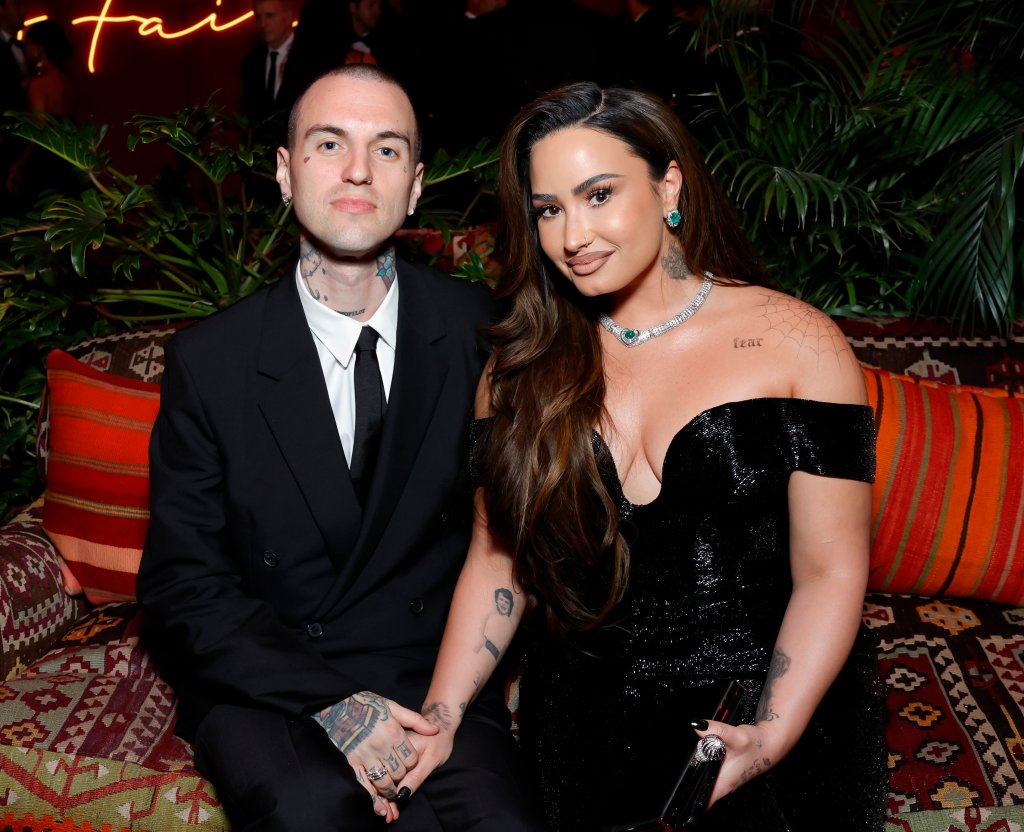 Jordan Lutes e Demi Lovato; eles estão sentados posando para foto de mãos dadas e sorrindo levemente