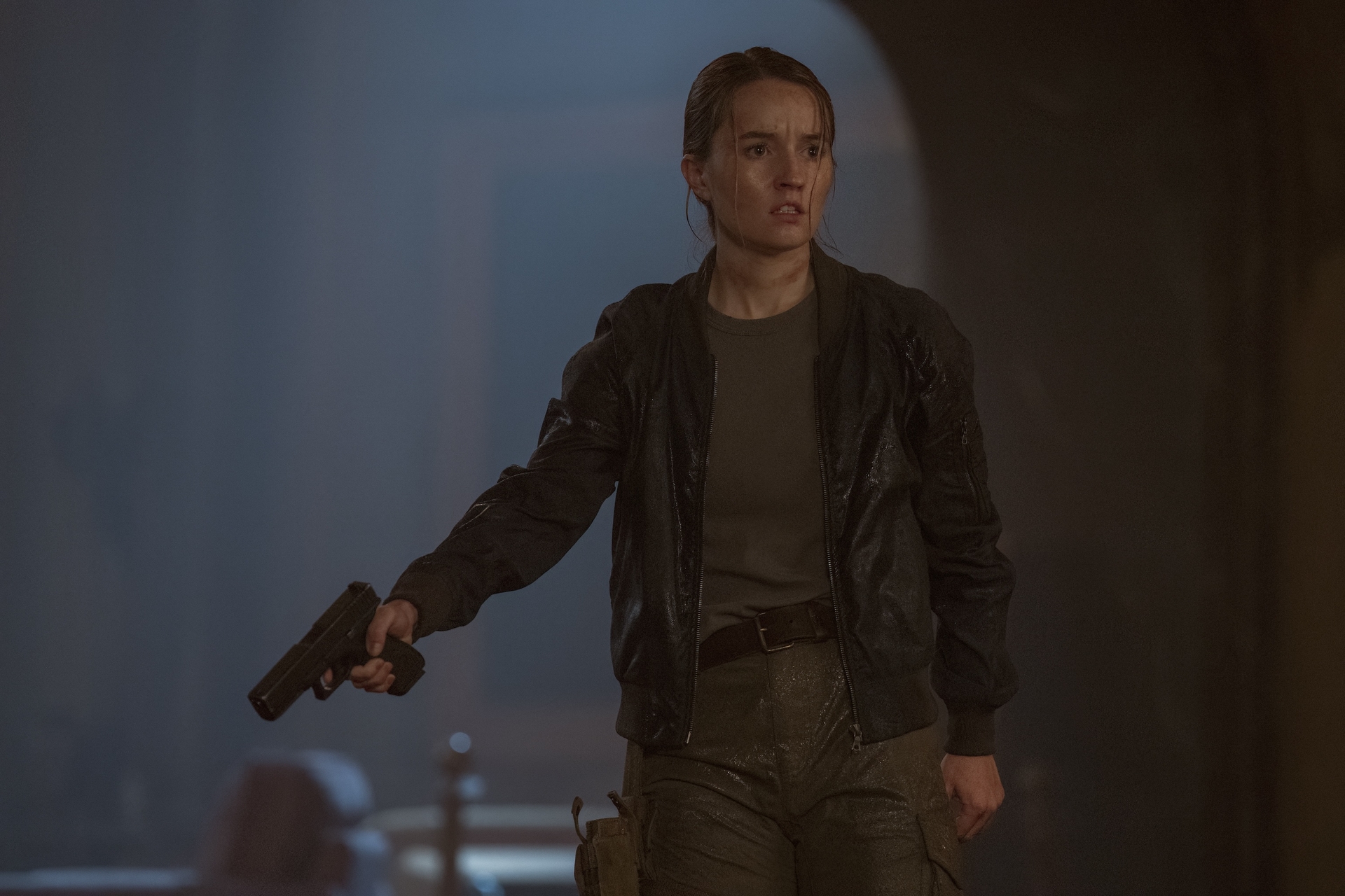 Kaitlyn Dever como Abby em cena de The Last of Us; ela está apontando uma arma
