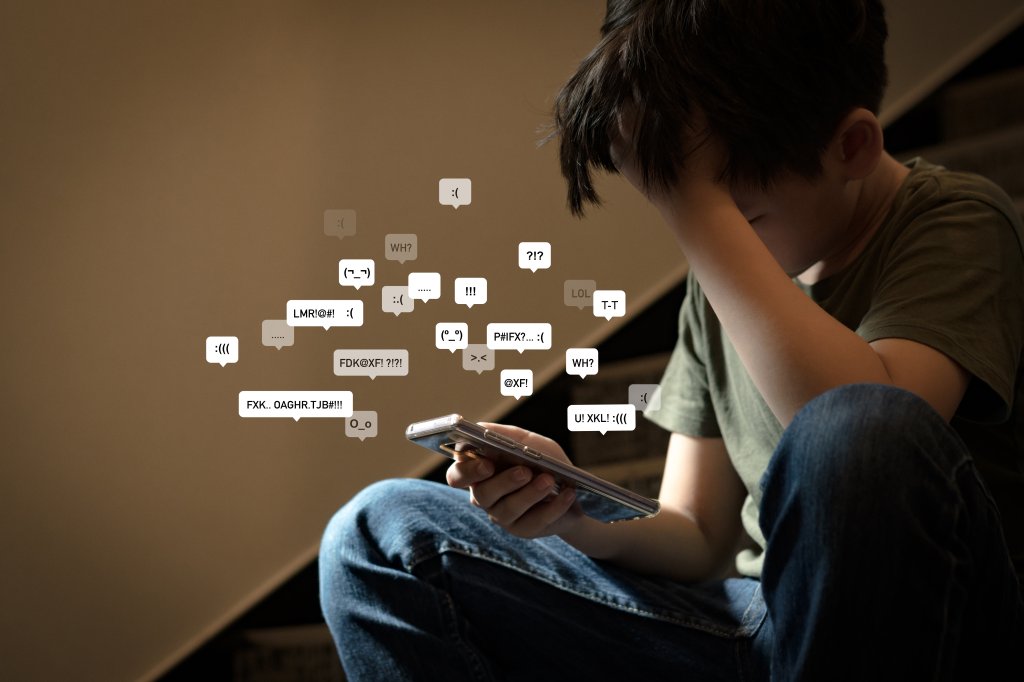 Adolescente asiático sentado em uma escada, cobrindo o rosto com as mãos, com o rosto para baixo, segurando o smartphone em um ambiente com pouca luz, sentindo-se frustrado, solitário, estressado e deprimido. Conceito de cyberbullying.
