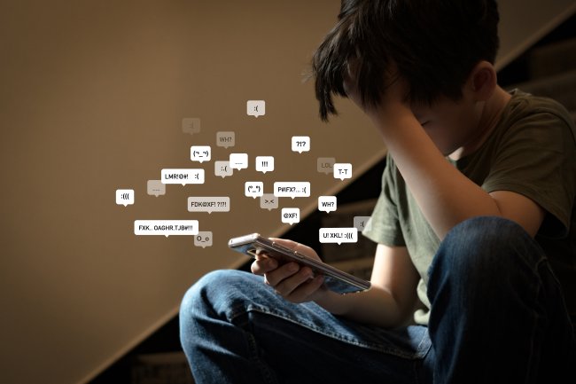 Adolescente asiático sentado em uma escada, cobrindo o rosto com as mãos, com o rosto para baixo, segurando o smartphone em um ambiente com pouca luz, sentindo-se frustrado, solitário, estressado e deprimido. Conceito de cyberbullying.