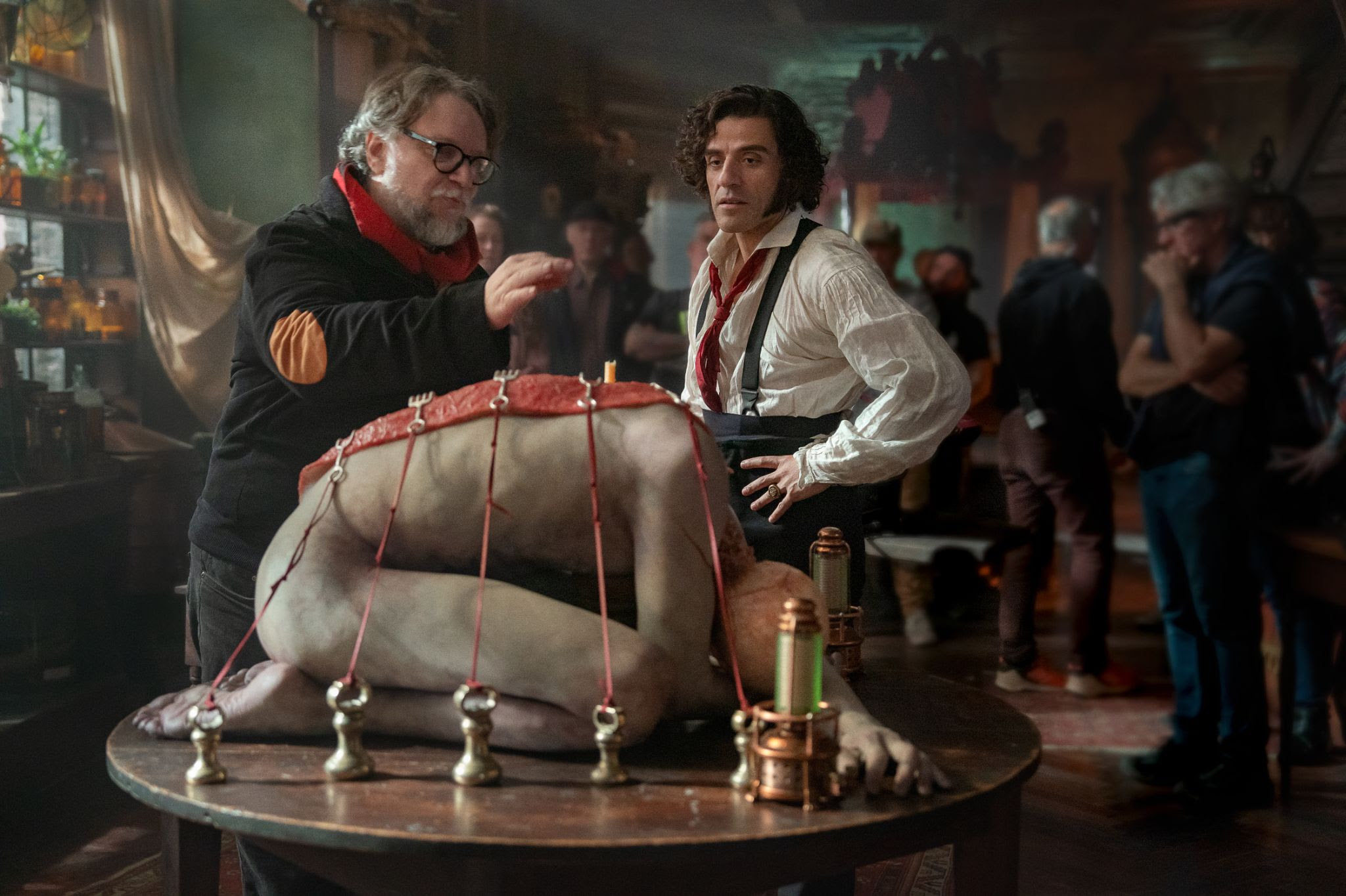 Oscar Isaac em Frankenstein Oscar Isaac surge ao lado do diretor do projeto, durante o ensaio de uma cena. Na imagem, os dois conversam, enquanto observam o corpo do monstro amarrado em uma mesa