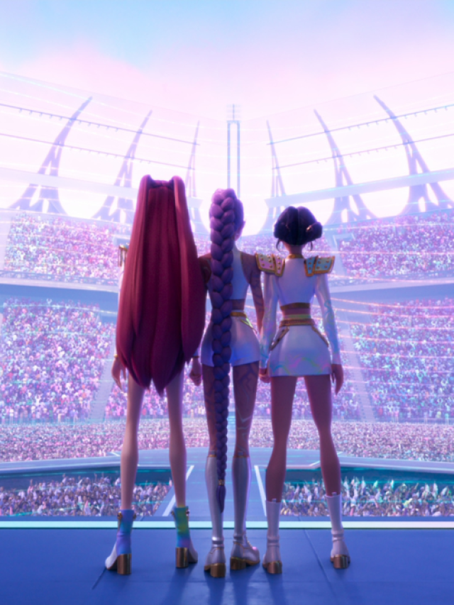 Três personagens animadas vistas de costas estão em um palco futurista, olhando para um enorme estádio lotado de público. Elas usam figurinos brilhantes e coordenados, com botas de salto e detalhes metálicos, enquanto luzes coloridas iluminam a cena em tons pastel, criando um clima de show grandioso e pop.