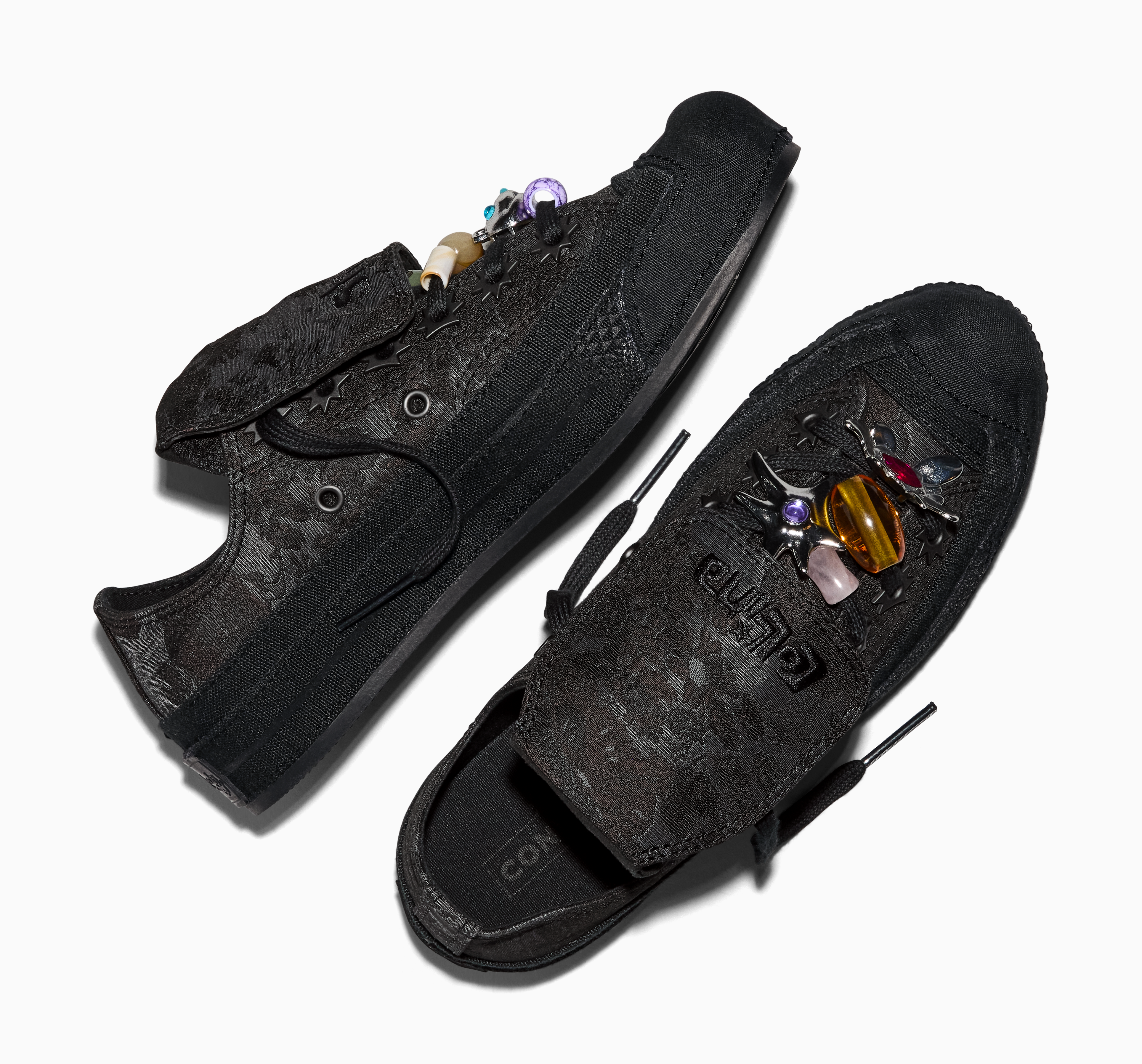 Par de tênis Converse pretos com estampa floral em relevo, um com pingentes de contas coloridas nos cadarços e outro com broches de insetos e pedras preciosas na lingueta