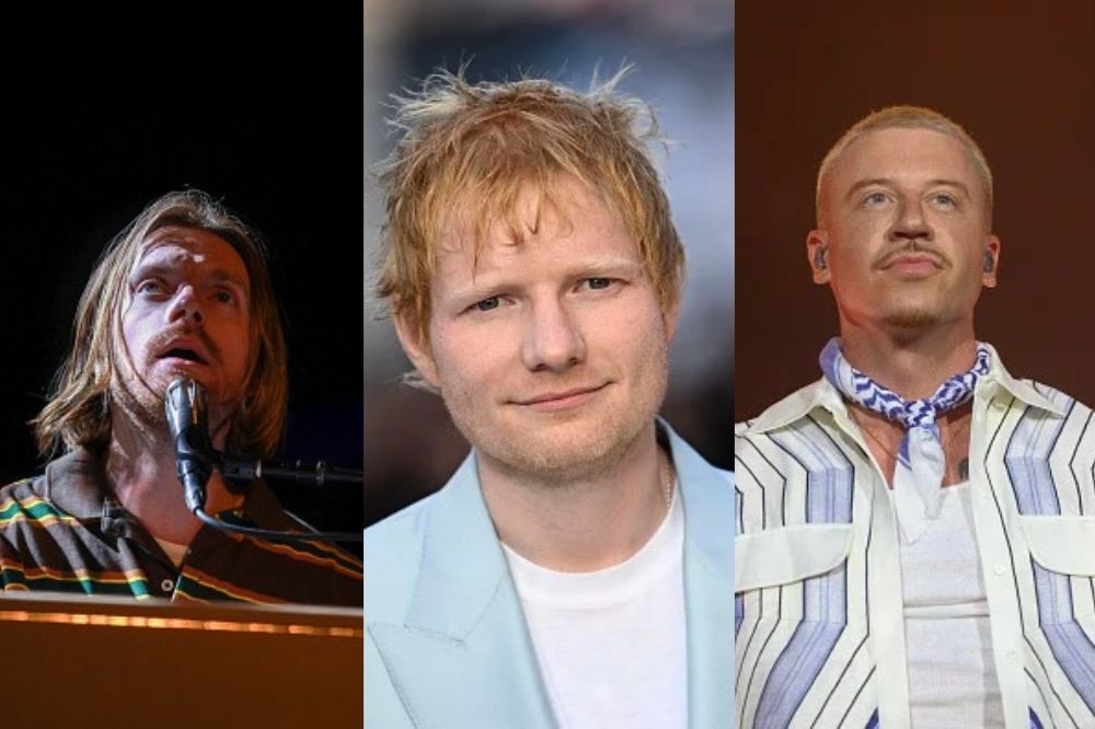 Três homens brancos em close-up: à esquerda, um homem de cabelo castanho comprido cantando em um microfone; ao centro, Ed Sheeran sorrindo levemente com cabelo ruivo bagunçado e blazer azul claro; à direita, um homem de bigode e cabelo loiro platinado usando camisa listrada e lenço azul no pescoço