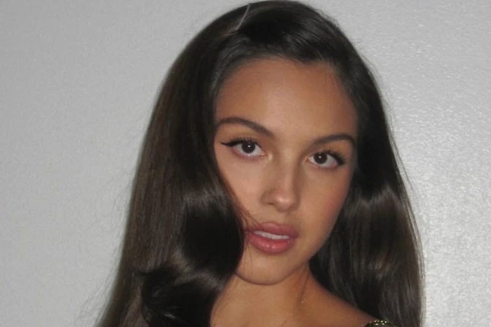 Rosto de uma mulher jovem com cabelo castanho escuro solto, maquiagem leve nos olhos e lábios rosados, olhando diretamente para frente