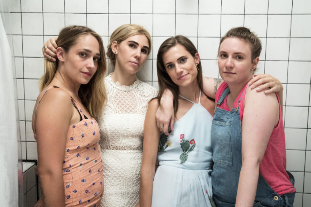 Quatro mulheres jovens posam juntas, sorrindo levemente para a câmera, em frente a uma parede de azulejos brancos. Da esquerda para a direita: uma mulher de vestido pêssego com estampa floral, outra de vestido de renda branco, uma terceira de vestido azul claro com bordado de cactos e a última de macacão jeans sobre uma blusa rosa. Elas se abraçam, demonstrando união.