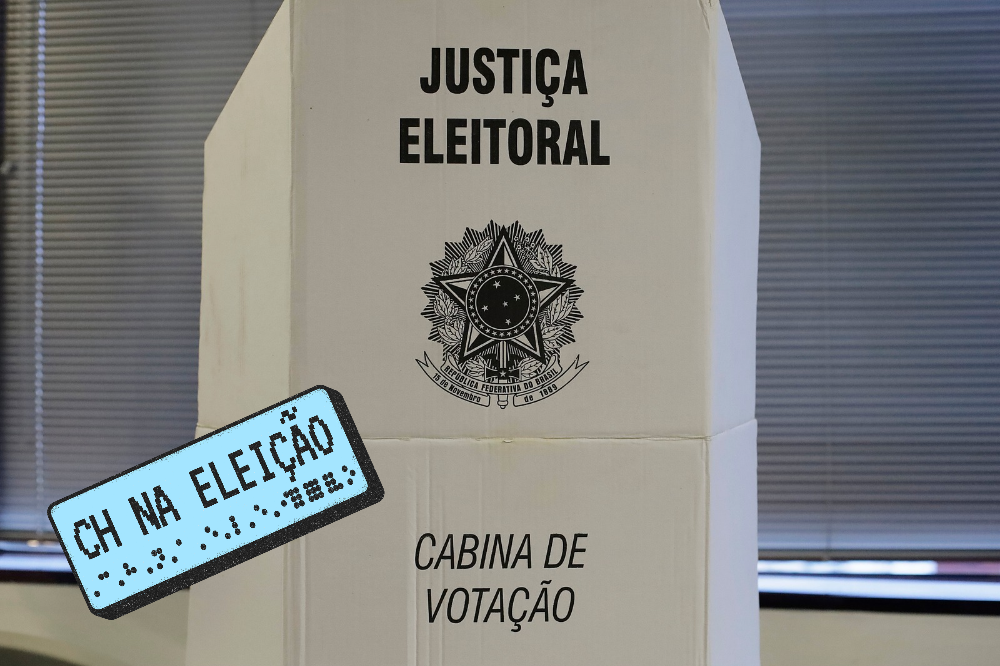 Cabine de votação branca com o texto JUSTIÇA ELEITORAL e o brasão da República do Brasil, e abaixo CABINA DE VOTAÇÃO. Uma placa azul com CH NA ELEIÇÃO e texto em braile está inclinada na frente.
